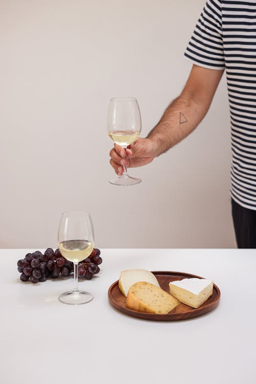Free A Person Holding a Wine Glass Near the Table with Foods Stock Photo