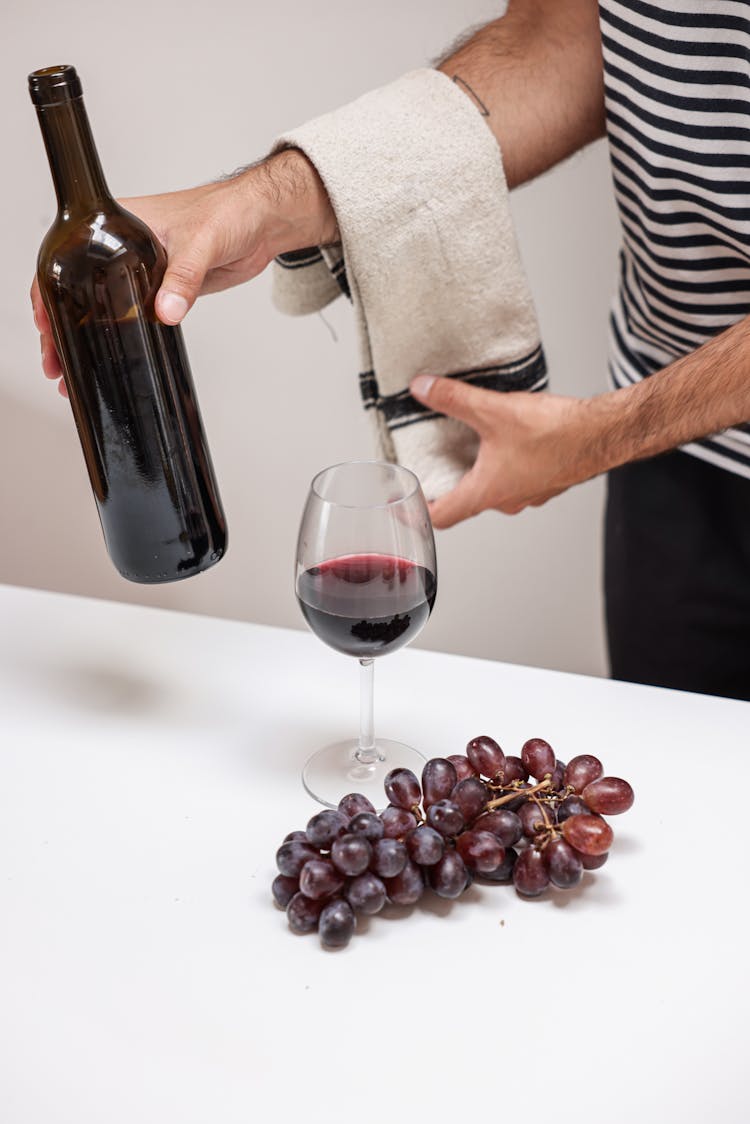 Man Holding A Bottle Of Wine By A Glass And Grapes