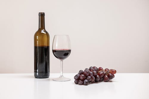 A Bottle of Wine Near the Wine Glass and Grapes on the Table