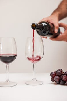 Red wine being poured into glass with grapes on table; a classic wine tasting scene.