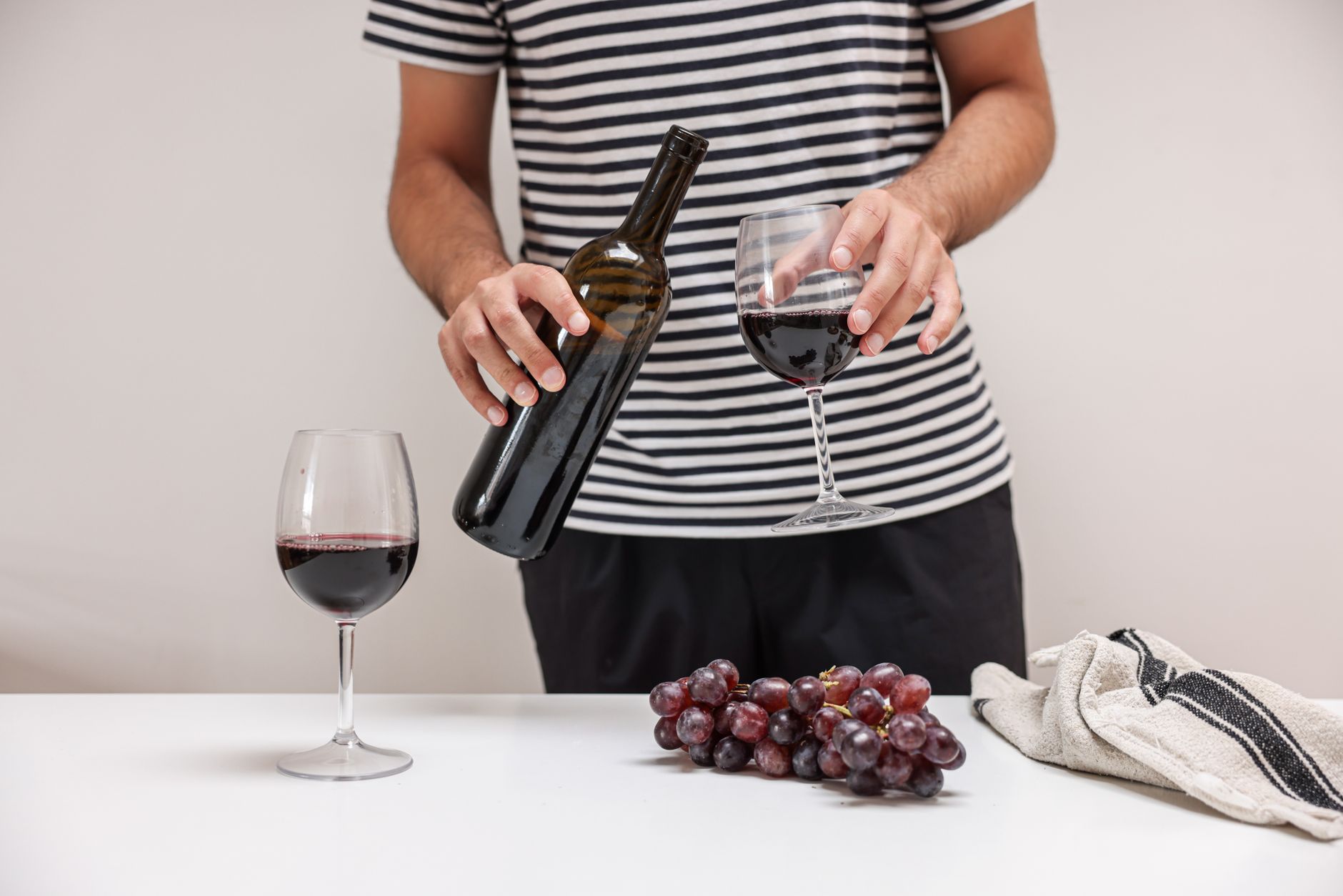 Adult pouring red wine into glass, grapes on table. Elegant and inviting indoor scene.