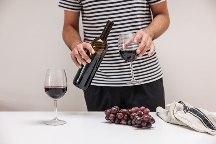 A Person In Striped Shirt Holding A Glass Bottle And A Glass Of Wine