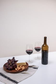 Elegant still life featuring red wine, cheese, and grapes on a table.
