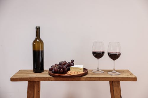 A Wine Bottle Near the Wooden Plate with Cheese and Grapes