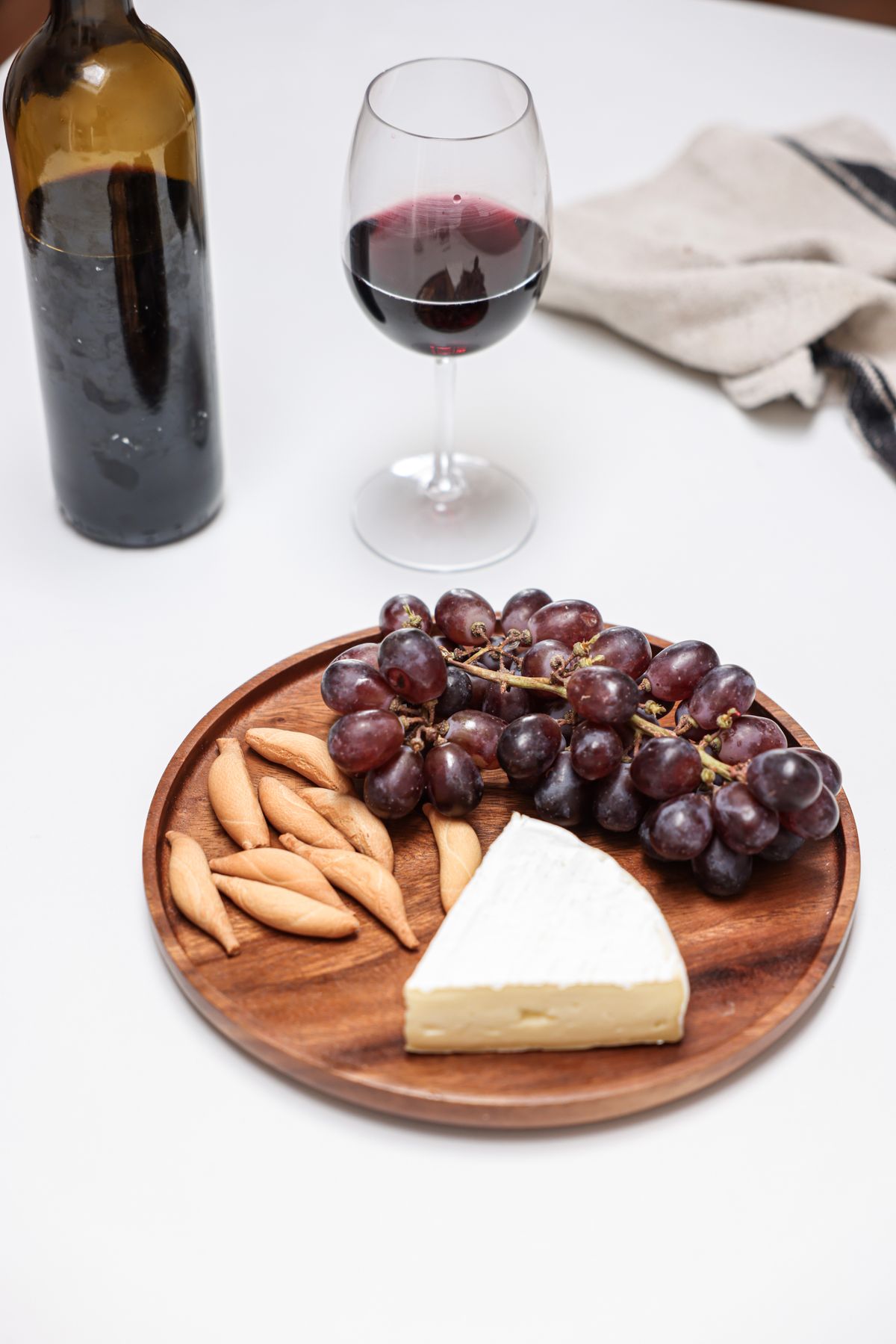 A wooden plate with cheese and grapes near a glass of wine on a table