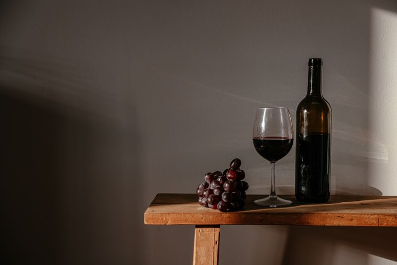 Poured glass of red wine beside a bottle and grapes — photo by Cup of Couple on Pexels