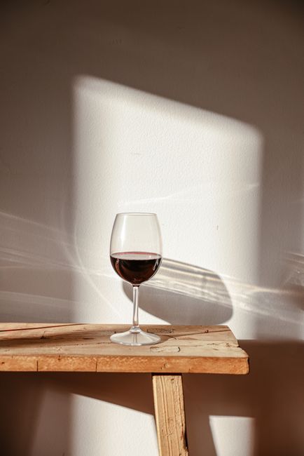 A glass of red wine casting a shadow on a wooden table in the warm sunlight.