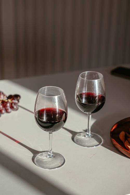 Free Elegant glasses of red wine on a sunlit table with grapes create a warm, inviting atmosphere. Stock Photo