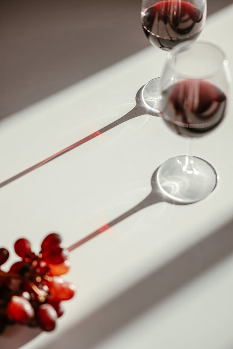 Wine Glasses And Grapes On White Surface