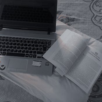 A cozy setup with an open book and laptop on a bedspread, perfect for study or work.