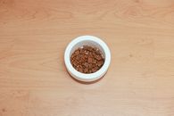 An overhead shot of dog food in a white bowl placed on a wooden floor, offering ample copy space.