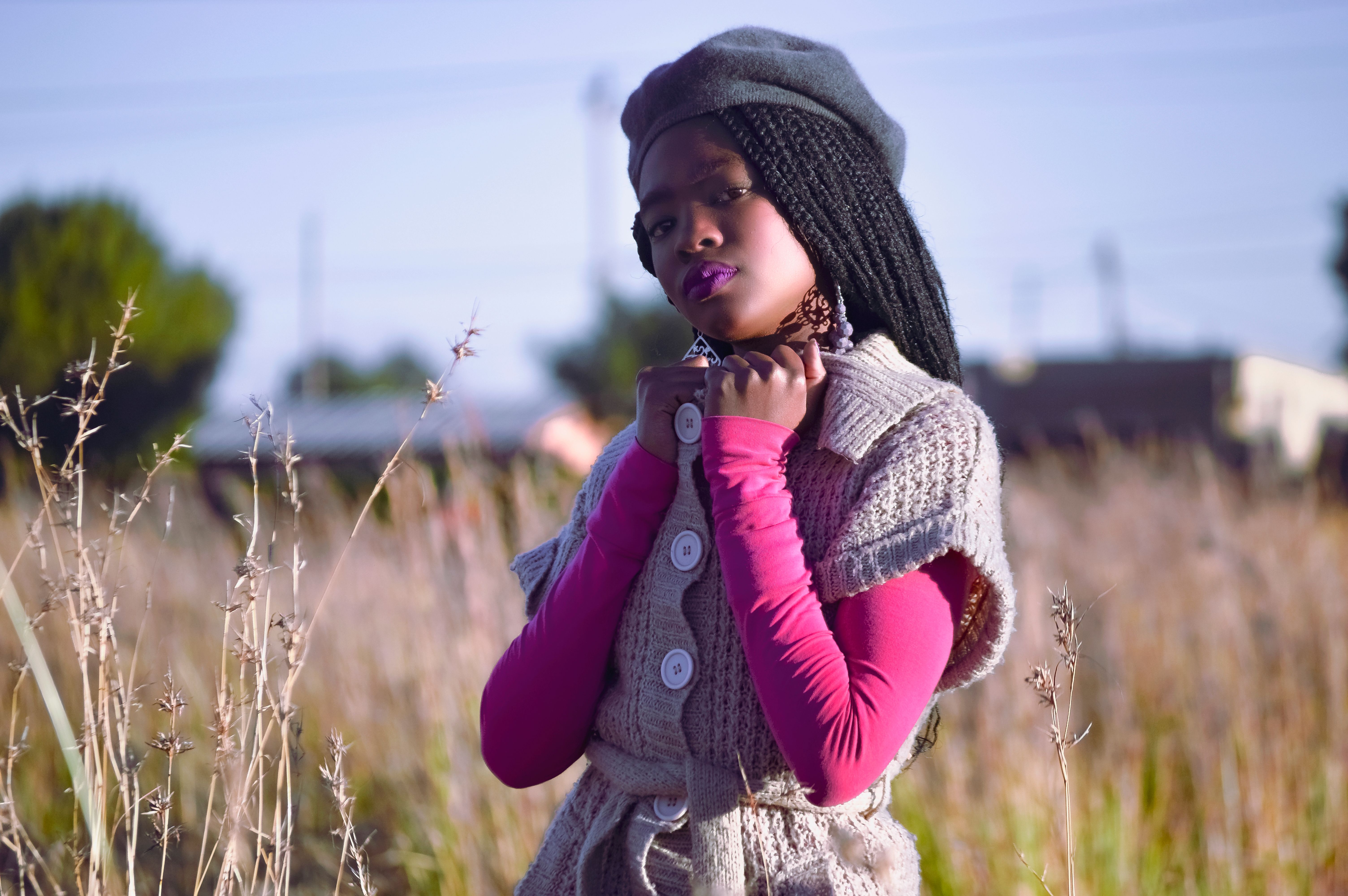 An African woman stands confidently in a field, dressed in cozy winter clothing