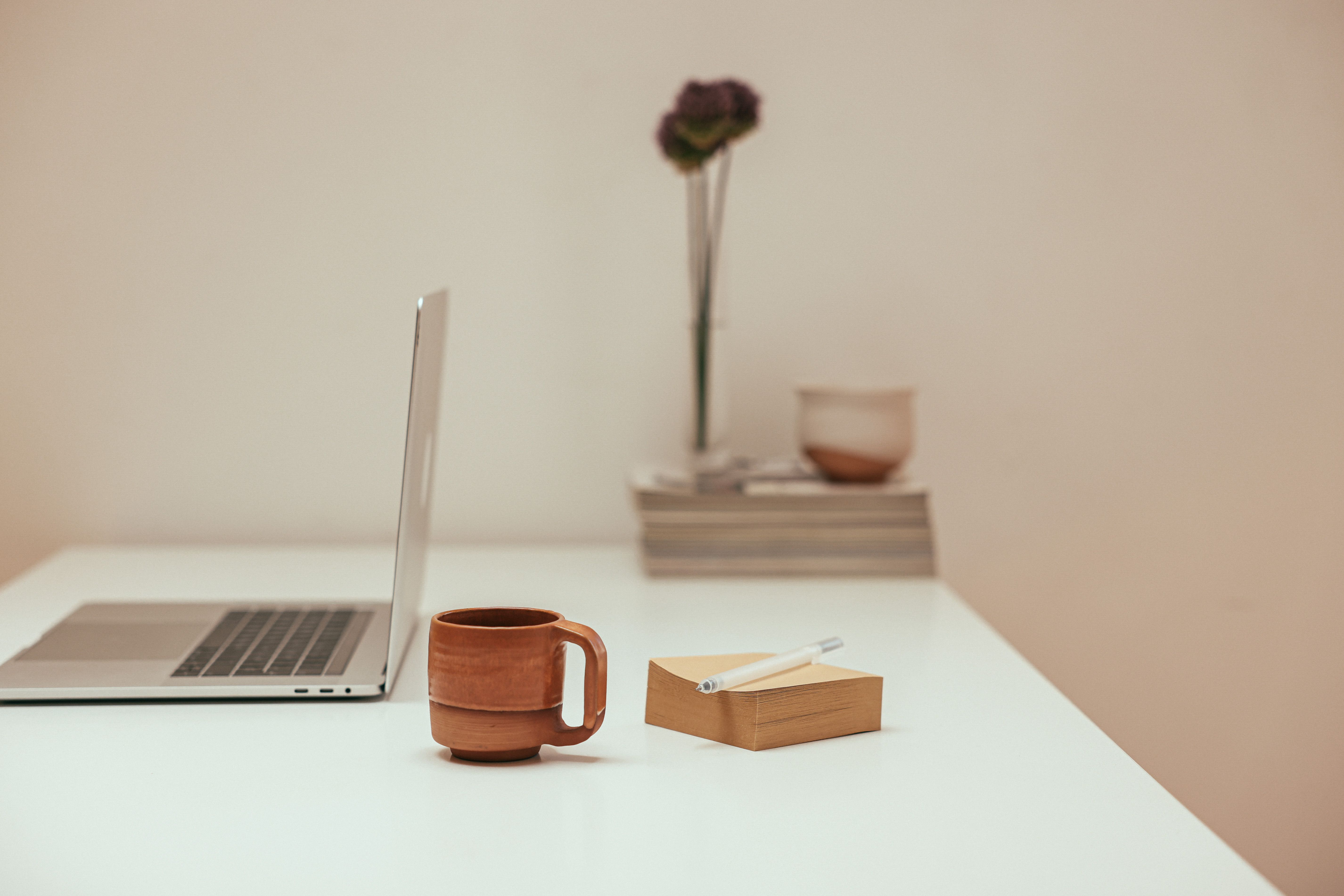Desk setup for a small space reset routine with a laptop, mug, pen, and notepad on a white desk.