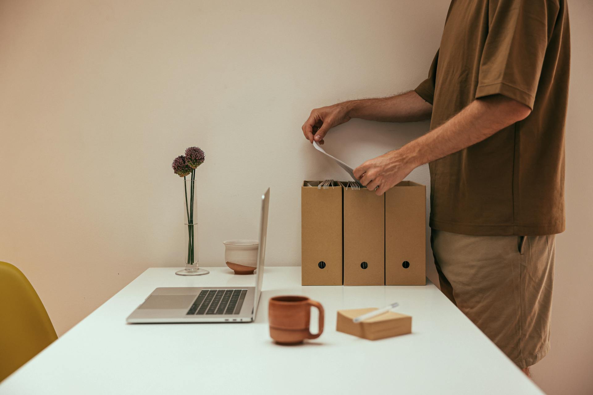 Man organizing papers in a minimal home office with white table and laptop.