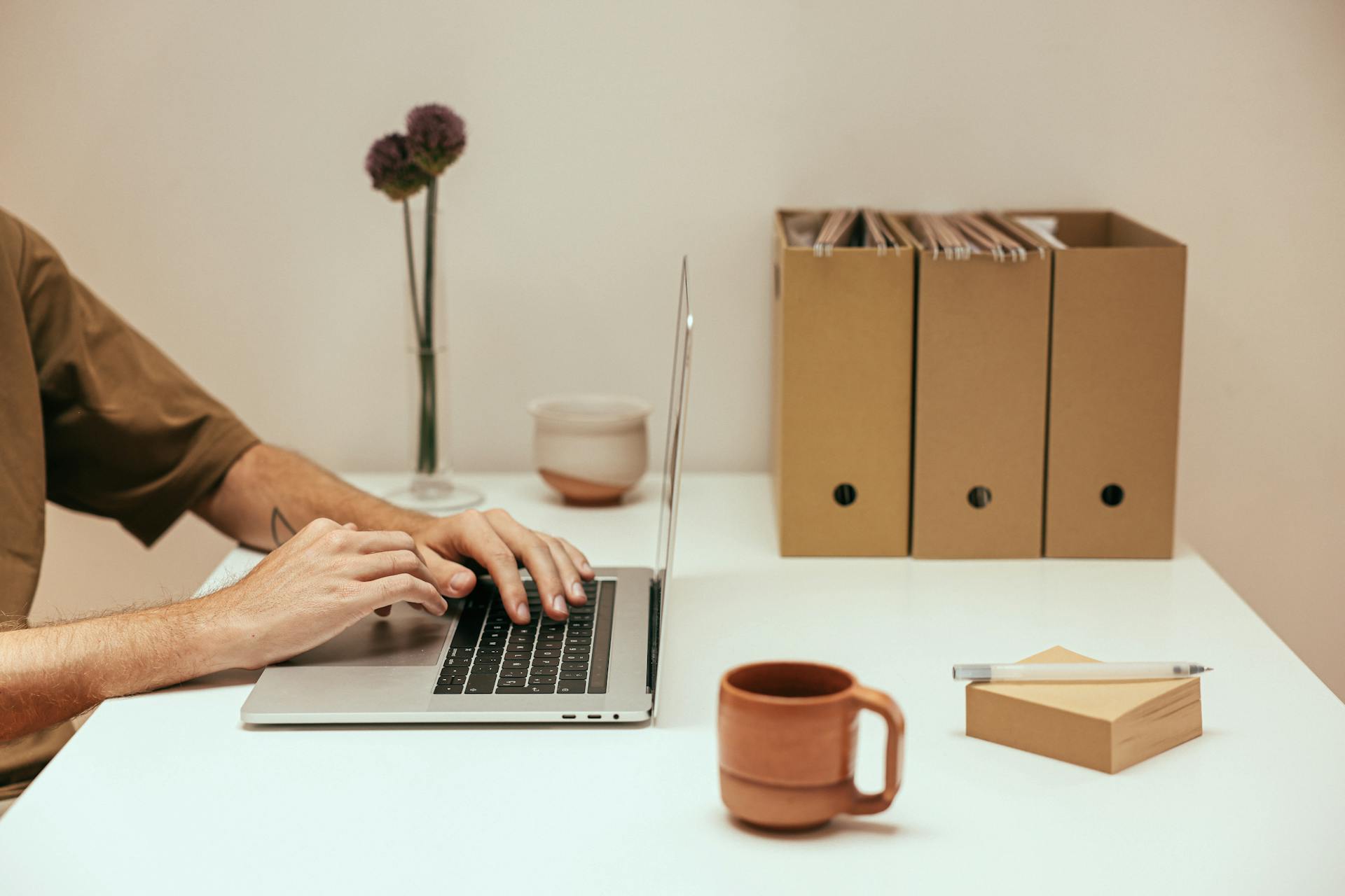 Hands typing on a laptop in a minimalist workspace with coffee and file organizers.