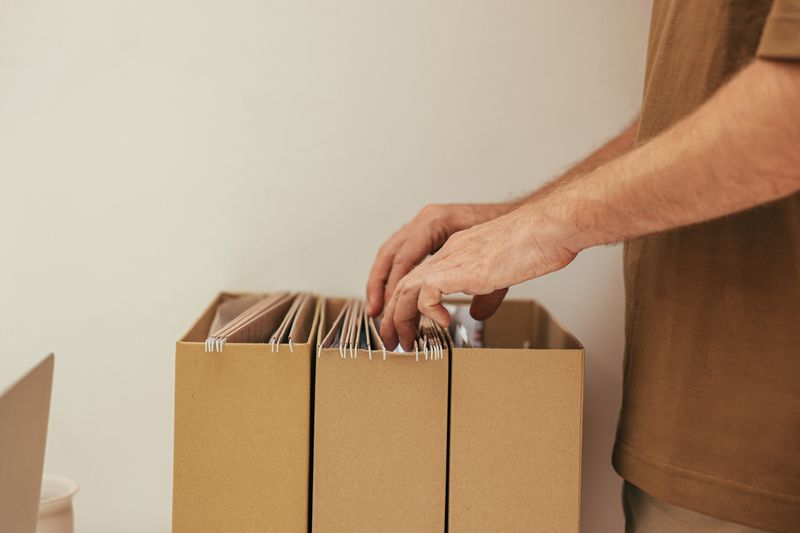 Hand sorting through hanging file folders in cardboard organizer boxes