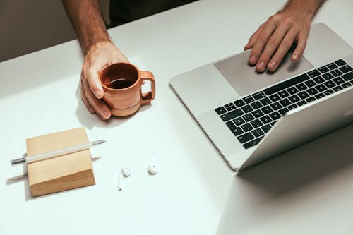 Una Persona Che Beve Una Tazza Di Caffè Mentre Usa Un Laptop