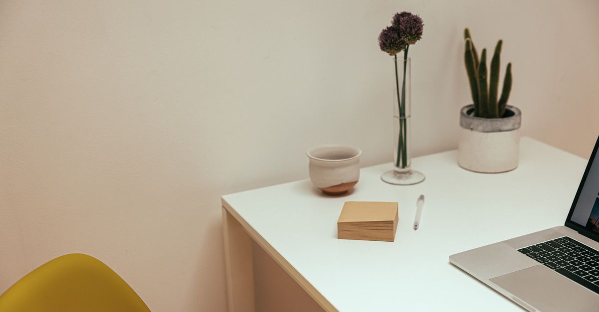 A clean and modern minimalist desk setup with a laptop, plants, and a ceramic cup.