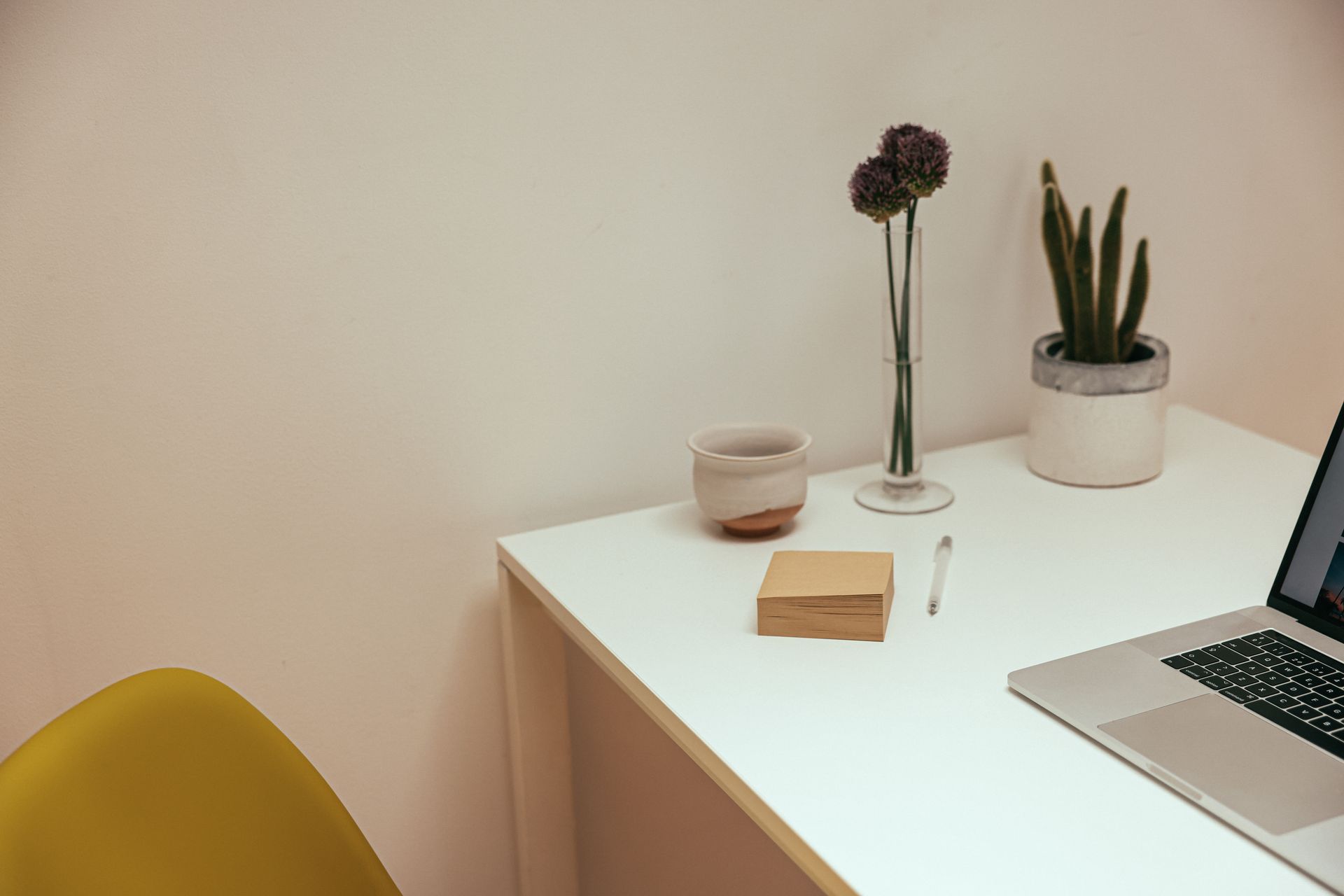 A clean and modern minimalist desk setup with a laptop, plants, and a ceramic cup.