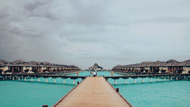 Scenic view of wooden pathway leading to overwater villas in Maldives on a cloudy day.