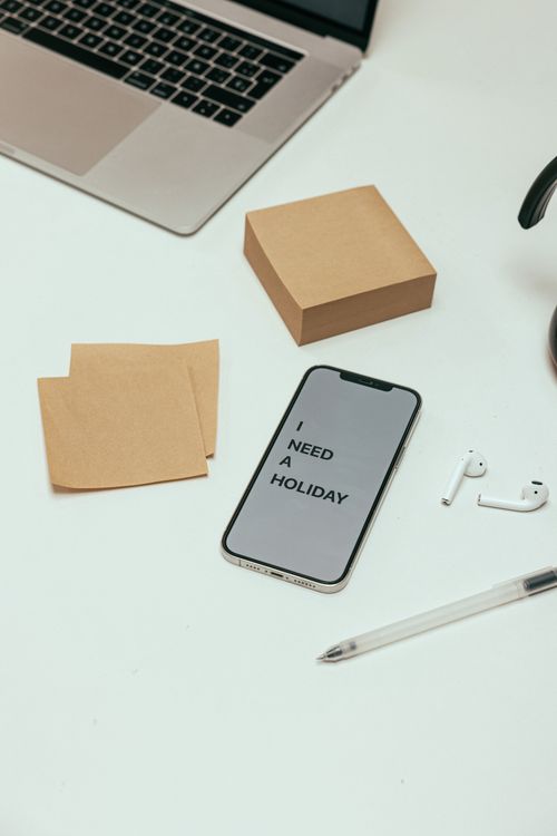 Free A cluttered desk with gadgets and 'I need a holiday' message on smartphone. Stock Photo