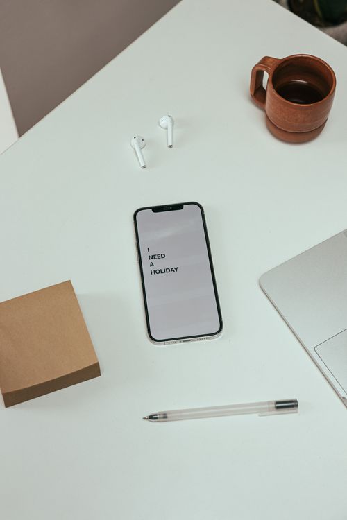 Free Overhead view of a desk with a smartphone, coffee mug, AirPods, and a notebook, conveying a modern work setup. Stock Photo