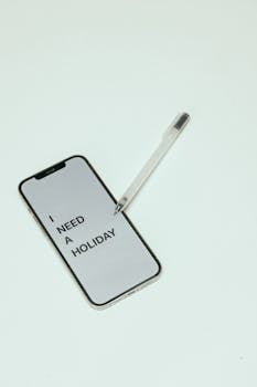 A smartphone with a text message reading 'I Need a Holiday' on a white background alongside a pen.