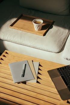 Warm indoor workspace scene with coffee, laptop, and notebooks on a wooden table.