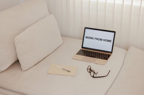 Free Minimalist workspace on a bed featuring a laptop, notepad, and glasses for remote work. Stock Photo