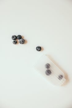 Overhead view of fresh blueberries scattered on a white surface next to a clear pouch, emphasizing simplicity and freshness.