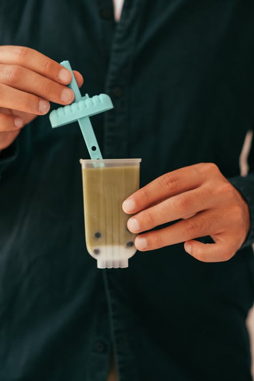 Person Holding a Plastic Popsicle Mold with Brown Liquid