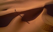 日落时分，一个孤独的身影走过沙丘，在沙漠中投下长长的影子