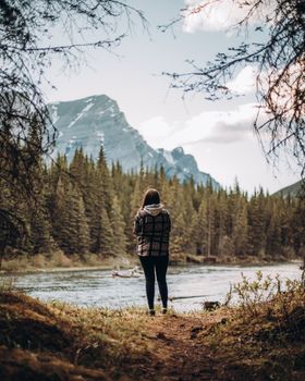Person standing in serene Kananaskis forest with mountain and river view.