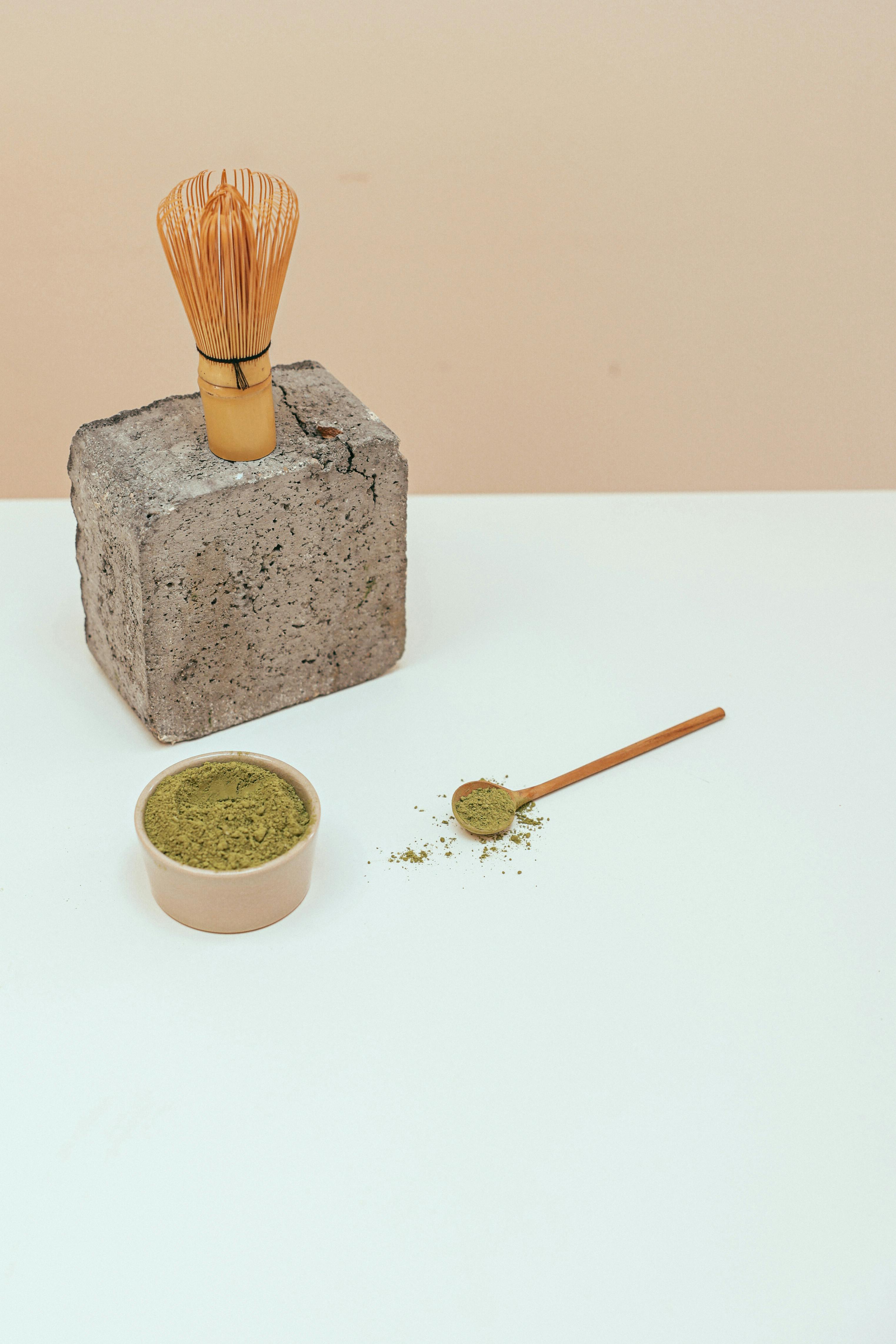 Stylish arrangement of matcha powder with a bamboo whisk on minimalist background.