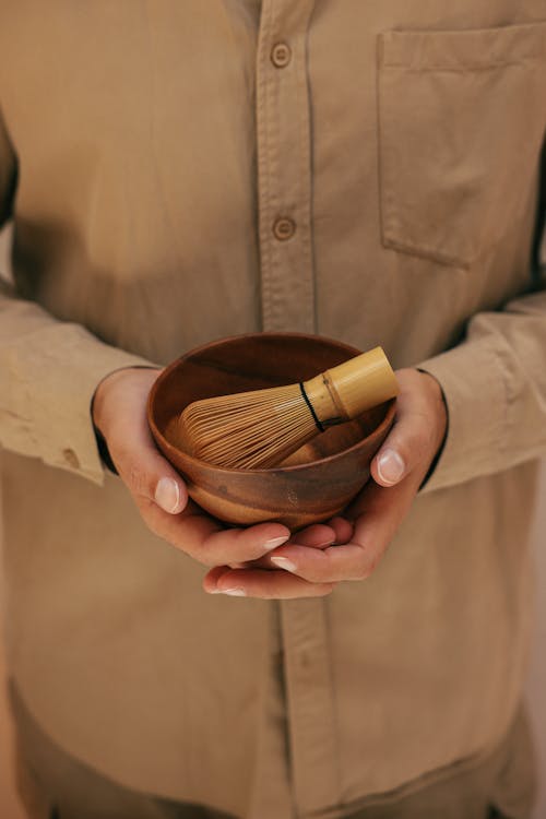 A Person Holding a Wooden Bowl with a Bamboo Whisk
