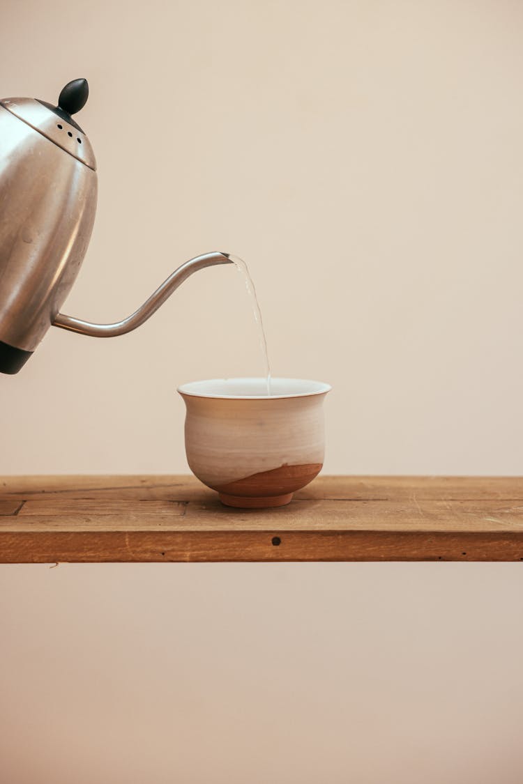 Water  From Teapot Being Poured Into A White Ceramic Cup 