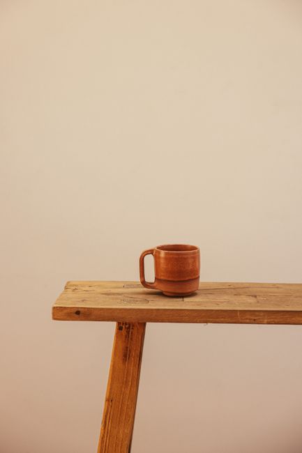 A simple brown ceramic mug placed on a rustic wooden table against a plain backdrop.
