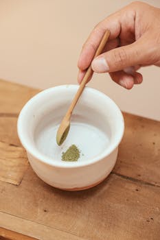 Close-up of matcha powder in a white bowl with a wooden spoon, ideal for zen and wellness themes.