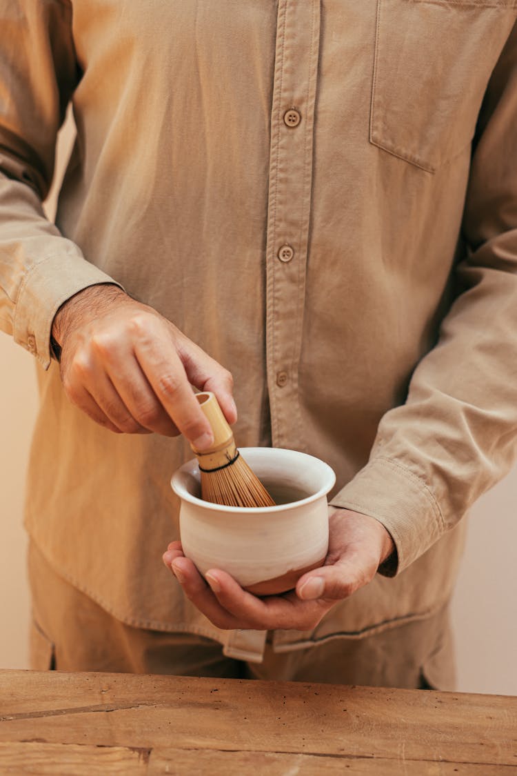 Person In Brown Long Sleeve Shirt Mixing Tea Using A Bamboo Whisk