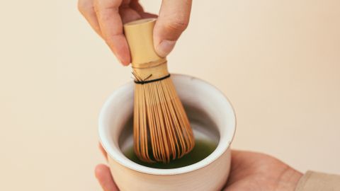 Close-up of bamboo whisk in hand mixing matcha tea for traditional Japanese tea ceremony.