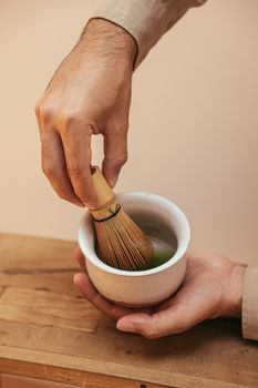 Close-up of a hand mixing matcha tea in a ceramic bowl using a bamboo whisk, embodying traditional tea ceremony.