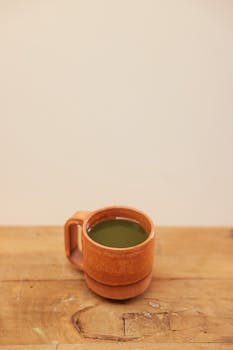 Aesthetic shot of a green matcha tea in a rustic ceramic mug placed on a wooden table.