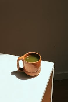 Ceramic mug with matcha latte on a sunlit white table, perfect for calming moments.