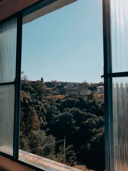 View of a scenic landscape with houses and trees through an open window on a sunny day.