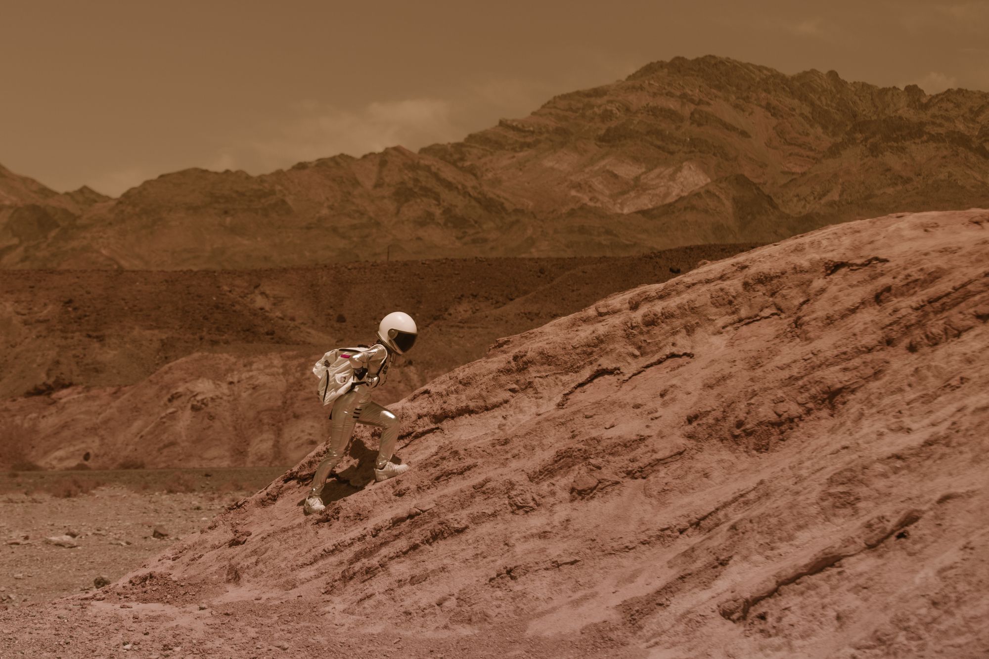 Astronaut in a spacesuit explores a desert-like environment with rocky formations.