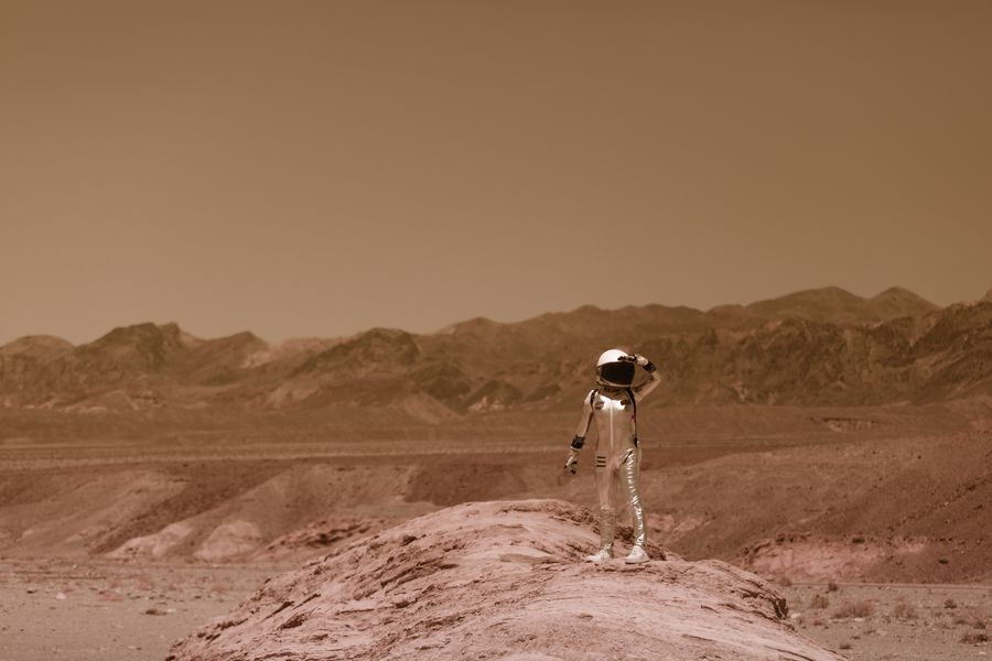 A figure in a pressure suit alone on rust-coloured desert ground — photo by RDNE Stock project on Pexels