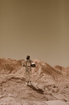 Astronaut in a space suit standing in a barren desert with rock formations.