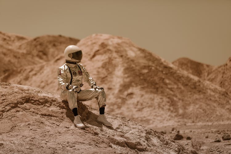 A Man In Space Suit Sitting On A Rock