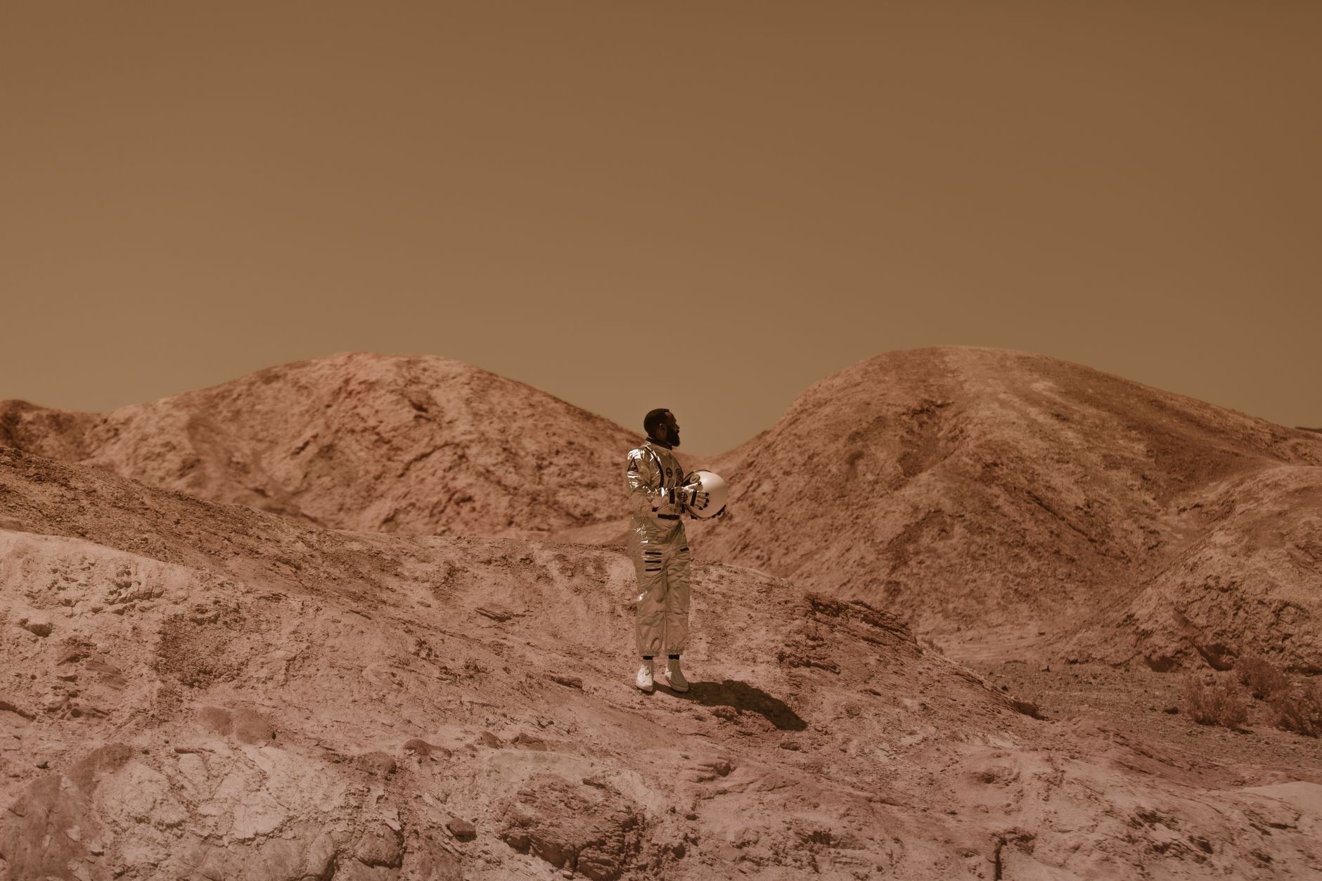 A man in a space suit stands in a barren, desert-like landscape, evoking a sense of exploration.