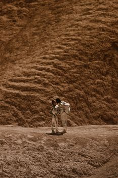 A couple in spacesuits embraces on a barren, alien-like rocky terrain, evoking themes of space exploration and romance.